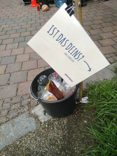 Ein Eimer mit Müll. Darüber befindet sich ein Schild mit der Aufschrift „Ist das deins?“