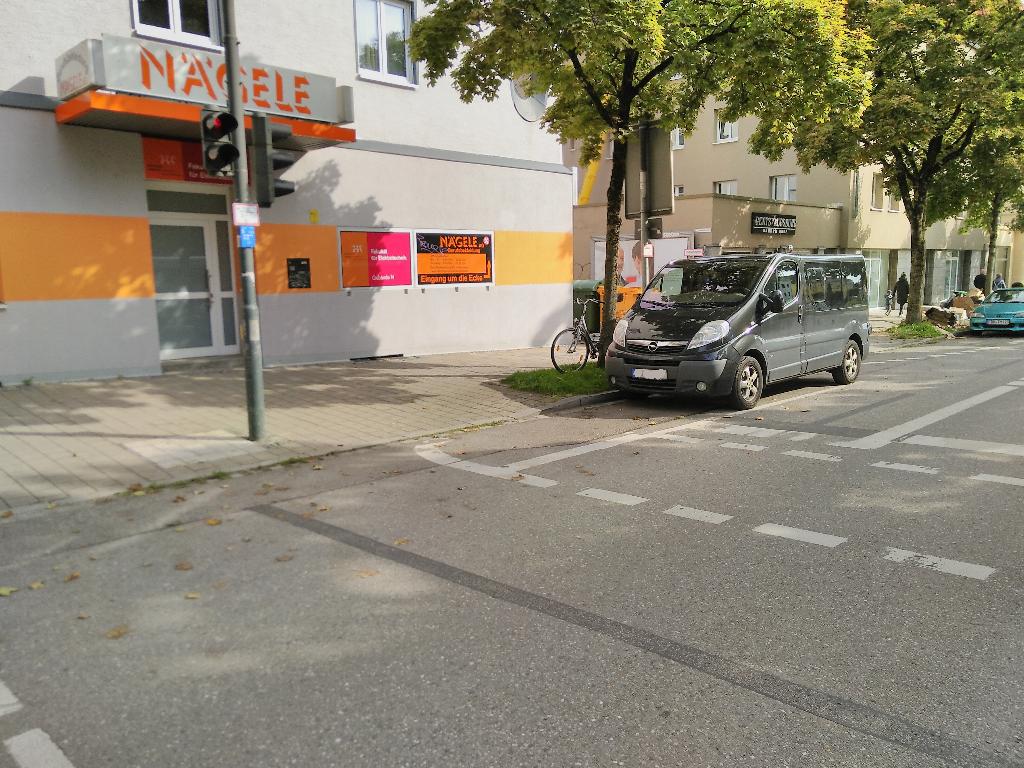 Das Foto zeigt einen schwarzen Kleinbus, möglicherweise von Opel, der auf dem Wartestreifen für linksabiegende Fahrradfahrer*innen unmittelbar vor einer Ampel parkt. Das Nummernschild ist verpixelt.