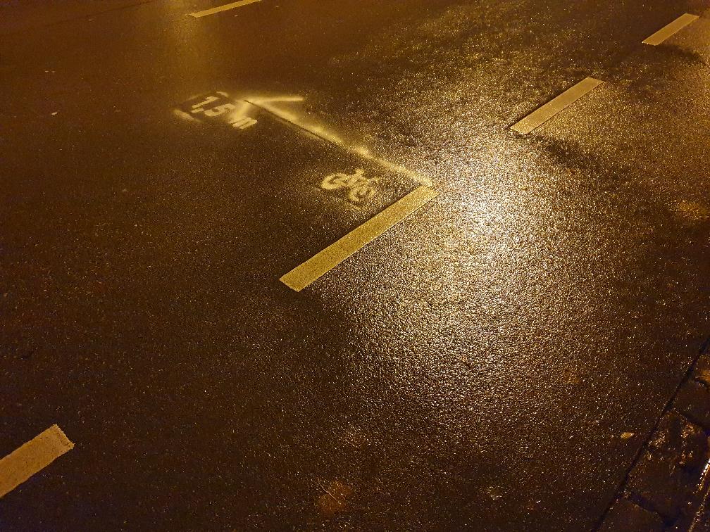Das Bild zeigt auf die Straße gesprüht, einen 1,5 Meter langen Pfeil, der senkrecht vom Radweg in die Mitte der Straße zeigt. Unterhalb des Pfeilfusses ist ein Fahrradsymbol aufgesprüht. An der Pfeilspitze steht „1,5 m“.