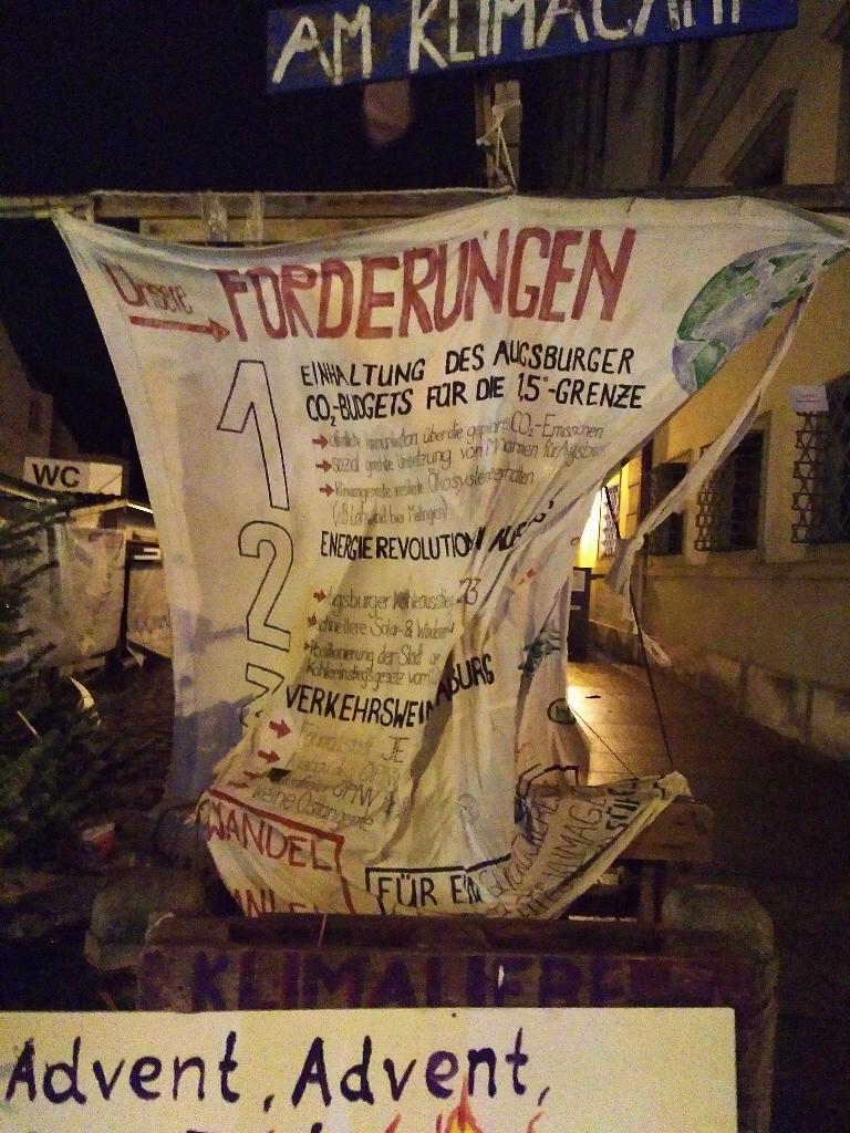 Das Bild, aufgenommen am Abend des 22.12.2022, zeigt das zerfetzte Banner mit den Forderungen, welches gewöhnlich an der Westseite des Klimacamps in Richtung Rathausplatz hängt.