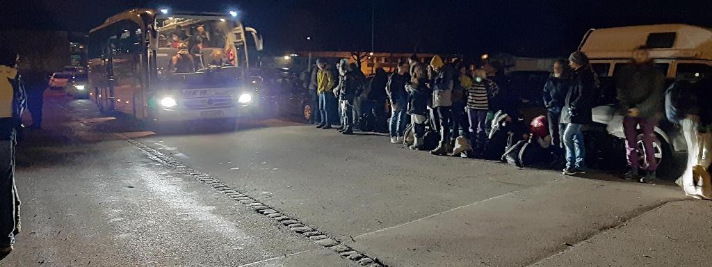 Das Bild zeigt zahlreiche Menschen, die eine Gasse für einen Bus bilden, der sich gerade zur Abfahrt bereit macht.