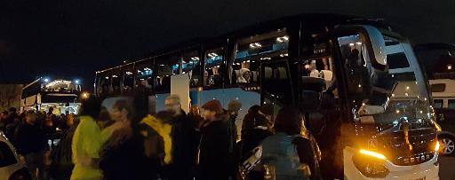 Eine große Gruppe von Menschen steht vor zwei anderen Bussen und wartet darauf einsteigen zu können. Innen sitzen bereits mehrere Menschen.