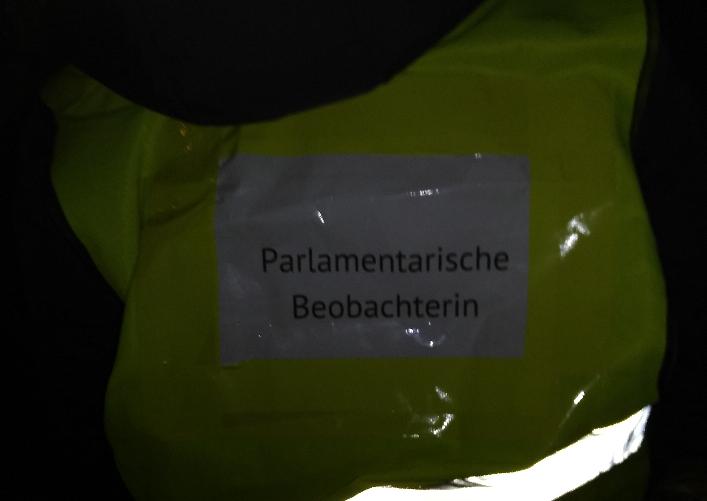 Das Bild zeigt die Rückseite einer gelben Warnweste mit der Aufschrift „Parlamentarische Beobachterin“.