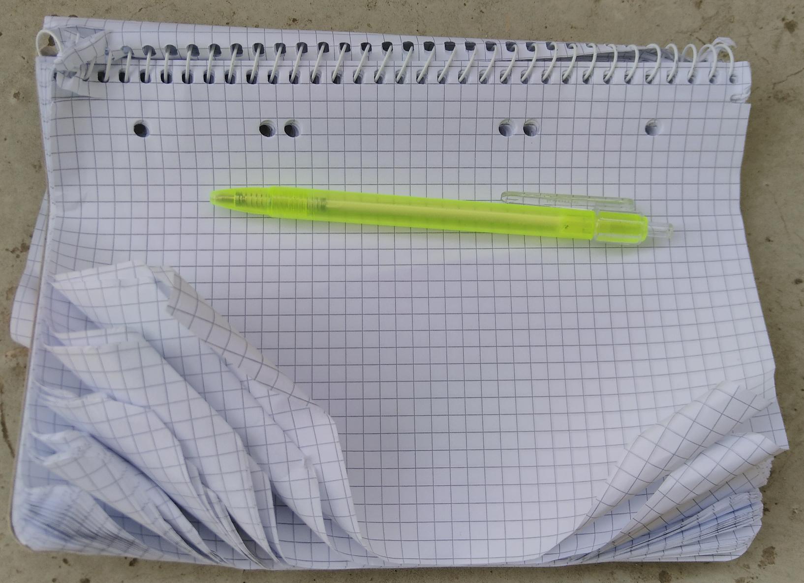 Das Bild zeigt einen verknitterten Block mit kariertem Papier sowie einen billigen Kugelschreiber aus Plastik.