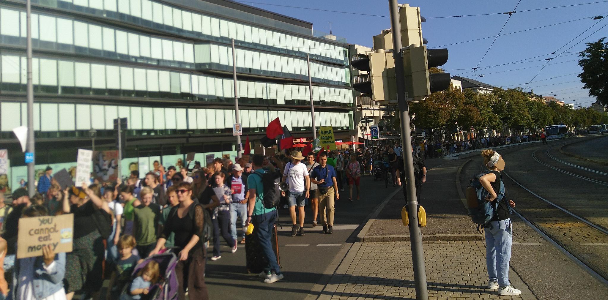 Von der Spitze der Demonstration am Kennedy-Platz nahe des Staatstheaters ist das Ende der Demonstration nicht zu erkennen. Fahnen und Pappschilder mit unterschiedlichen Schriftzügen ragen des der Demonstration.