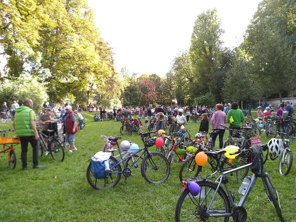 Auf einer Wiese in der Grünanlage an den Wallanlagen neben dem Spitalbach stehen Fahrräder und Gruppen von Menschen. Die Fahrräder sind mit Luftballons und Bannern verziert. Die Wiese ist umgeben von großen Laubbäumen.