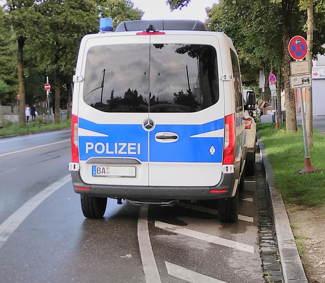Das Foto zeigt einen Einsatzwagen der bayerischen Bereitschaftspolizei, der im Halteverbot steht und so weit in den Radweg hineinreicht, dass Fahrradfahrer*innen auf die Straße ausweichen müssen. Die Autonummer wurde verpixelt.